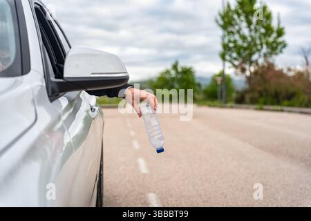 Un uomo che getta una bottiglia d'acqua di plastica usata fuori dalla sua auto e inquina l'ambiente Foto Stock