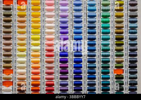 Colorate file verticali di bobine assortite di fili da cucire disposte per tonalità su un espositore in un negozio di tessuti Foto Stock
