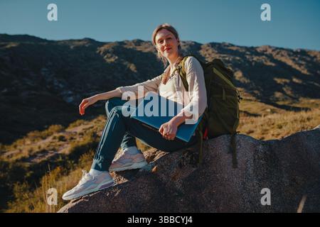 Giovane turista con zaino e laptop siede in cima alla montagna Foto Stock
