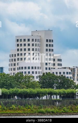Moderno edificio bianco di Frank Gehry con linee curve dietro gli alberi del fiume Foto Stock