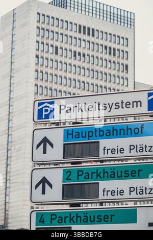 Diversi cartelli stradali e di parcheggio con un edificio per uffici sullo sfondo Foto Stock