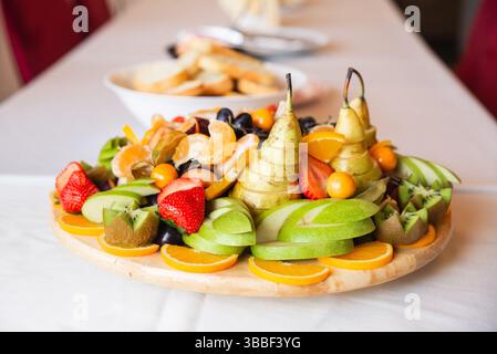 Un vivace vassoio di frutta con pere affettate, arance, kiwi, fragole e uva, organizzato splendidamente per un'occasione festiva. Foto Stock