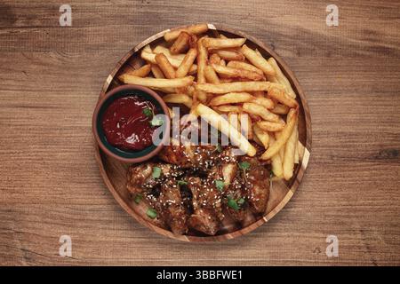 Ali di pollo alla griglia, cosparse di semi di sesamo, patatine fritte e salsa, su un piatto di legno, stile rustico Foto Stock