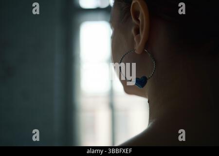 Primo piano di una persona che indossa un orecchino a forma di cuore blu Foto Stock