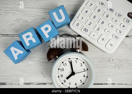 Testo ARPU (Average Revenue per User) con allarme clcok e calcolatrice su sfondo in legno Foto Stock