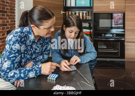 Madre e figlia ascoltano la radio a batteria durante il blackout elettrico in cucina Foto Stock