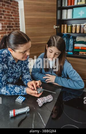 Madre e figlia ascoltano la radio a batteria durante il blackout elettrico in cucina Foto Stock
