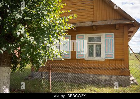 Una piccola casa con una recinzione bianca e un albero davanti. La casa ha molte finestre e un portico Foto Stock