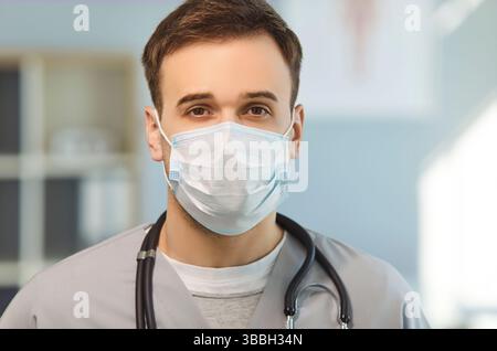 Ripresa interna di giovane uomo medico indossare maschera medica con stetoscopio che guarda la macchina fotografica seriamente Foto Stock