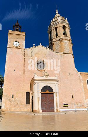 La chiesa di Sitges, in Spagna, si affaccia sul Mar Mediterraneo, con gente che cammina lungo il lungomare Foto Stock