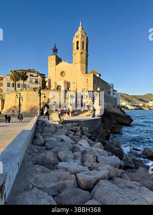 La chiesa di Sitges, in Spagna, si affaccia sul Mar Mediterraneo, con gente che cammina lungo il lungomare Foto Stock