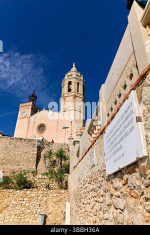 La chiesa di Sitges, in Spagna, si affaccia sul Mar Mediterraneo, con gente che cammina lungo il lungomare Foto Stock