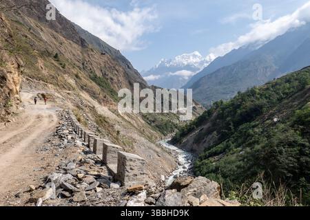 Strada sterrata e sentiero di trekking nella parte inferiore del circuito di Manaslu vicino a Jagat, Nepal. Picchi dell'Himalaya e gola del fiume in lontananza Foto Stock