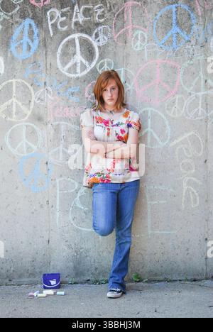 Giovane donna con atteggiamento si appoggia contro il muro coperto Graffiti Foto Stock