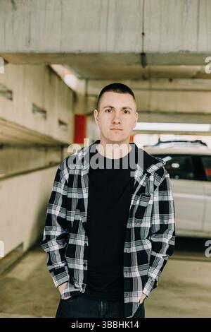 Giovane uomo in camicia a quadri in piedi nel parcheggio Foto Stock