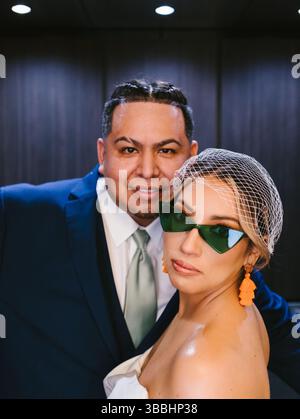 Sposa in velo da gabbia per uccelli, occhiali da sole verdi e orecchini di orang con sposo Foto Stock