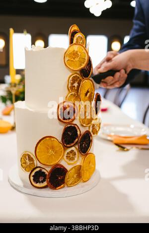 Torta nuziale bianca tagliata da sposi e sposi con dettagli agrumati Foto Stock