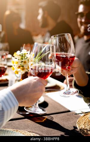 Gli amici brindano vino rosso in un pranzo informale all'aperto in una giornata di sole Foto Stock