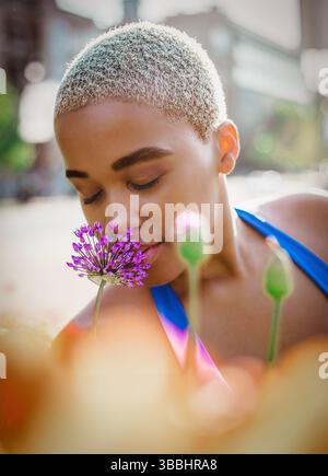 Una giovane donna nera che annusa delicatamente un fiore Foto Stock
