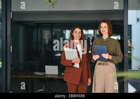 Due donne d'affari felici e sorridenti in piedi al lavoro in ufficio, ritratto. Foto Stock