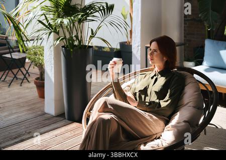 Giovane donna d'affari rilassata che fa una pausa di lavoro bevendo un caffè seduto sulla sedia. Foto Stock