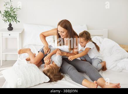 Una famiglia allegra giocosa felice che gioca a letto, che solletica i genitori e i bambini piccoli che ridono mentendo Foto Stock