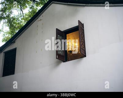 Lampadario di cristallo visibile attraverso la tradizionale finestra di lattice sulla casa di Hangzhou dipinta di bianco Foto Stock
