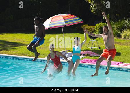 Saltando diversi amici tenendosi per mano e spruzzando in piscina nel cortile, con ombrellone e grigliate Foto Stock
