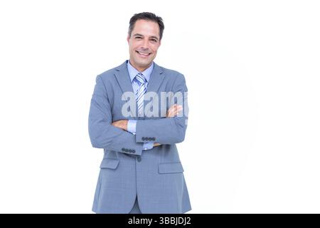 Un uomo di mezza età sorridente che incrocia le braccia sullo sfondo in studio, mostrando cravatta grigia a righe Foto Stock