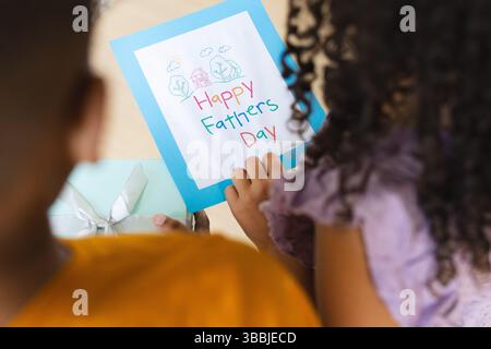 Due fratelli e sorelle che tengono in mano il biglietto per il giorno dell'Happy Fathers Day al tavolo di casa, con confezione regalo verde menta Foto Stock