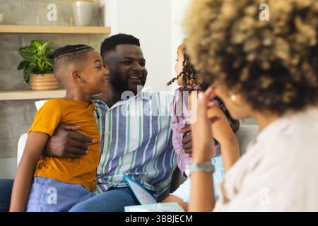 Lettura di diverse famiglie sul divano nel soggiorno, con libro illustrato aperto e pianta decorativa Foto Stock
