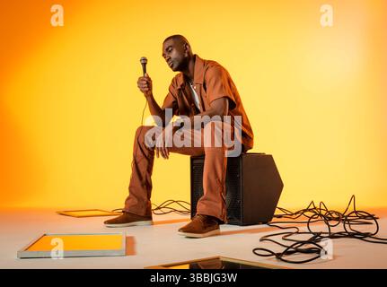 Uomo afroamericano seduto con microfono sull'altoparlante in studio, con cavi e riflettori Foto Stock