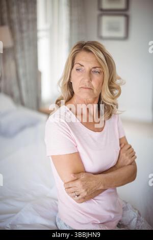 Donna anziana seduta che incrocia le braccia sul letto in camera da letto, mostra la fede nuziale e lo spazio per le copie Foto Stock