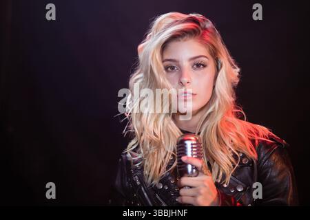 La cantante femminile tiene in mano il microfono vintage in uno studio con luce bianca e retroilluminazione rossa Foto Stock