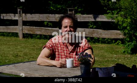 Uomo attraente che tiene una tazza di caffè in un parco al sole. Foto Stock