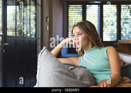 Donna ventenne appoggiata sul divano di casa mentre riposa la testa su un cuscino grigio, copia spazio Foto Stock