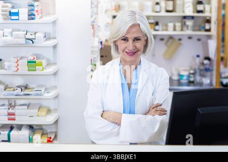 Farmacista senior sorridente in piedi dietro il bancone in farmacia, con bottiglie di farmaci Foto Stock