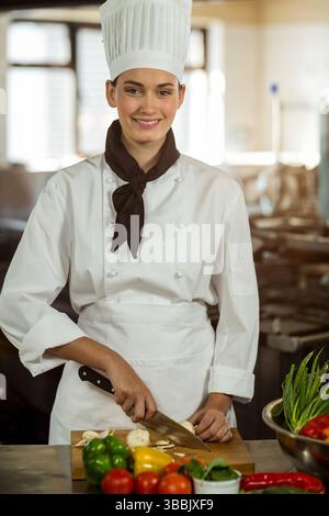 Affettare funghi da cuoca femminile utilizzando un coltello sul tagliere nella cucina commerciale, con verdure Foto Stock