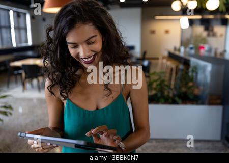 Giovane donna afroamericana che usa un tablet nella moderna sala d'ufficio, indossa uno smartwatch e sorride Foto Stock