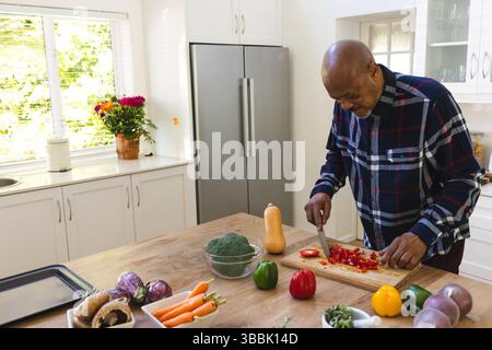Uomo anziano che trita peperoni rossi con coltello da cucina sul ripiano in cucina moderna, spazio per copiare Foto Stock