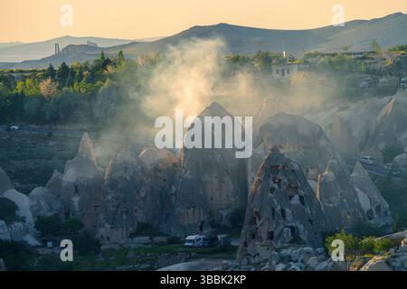 La nebbia mattutina sorge tra i camini delle fate e le vette rocciose della Cappadocia Goreme, creando un paesaggio mistico all'alba. Foto Stock