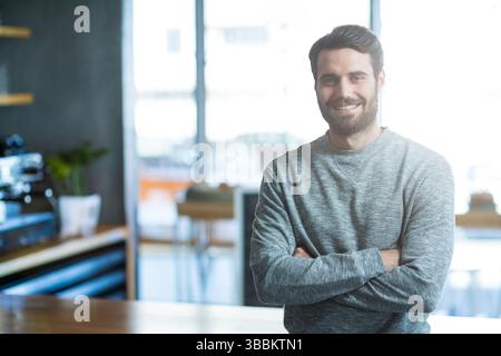 Uomo sorridente in piedi accanto al bancone di legno presso il moderno caffè, dotato di macchina per espresso commerciale Foto Stock