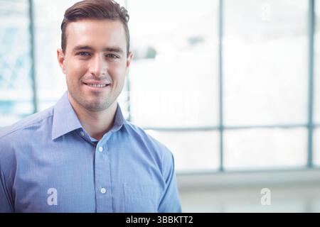 Uomo sorridente che indossa una camicia button-down azzurra in piedi in un moderno spazio ufficio, spazio fotocopie Foto Stock