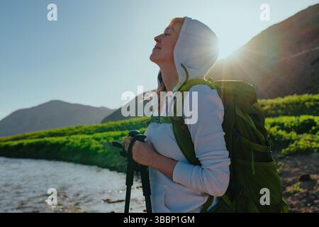 Donna felice escursionista a occhi chiusi che gode della natura alla luce del tramonto Foto Stock