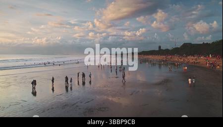 I turisti che camminano lungo la spiaggia sabbiosa di Dreamland Beach a Bali, Indonesia, vengono catturati in una vista aerea con un drone durante uno splendido tramonto, circondato da un cielo spettacolare e pieno di nuvole Foto Stock