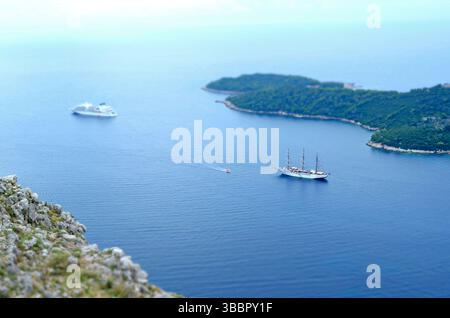 Vista aerea della nave da crociera e dell'alto veliero ancorati vicino alle isole verdi in un mare calmo e limpido, con scogliera rocciosa in primo piano Foto Stock