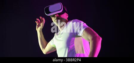 Uomo sportivo maturo che usa occhiali VR su sfondo scuro Foto Stock