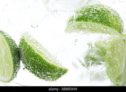 Rinfrescante acqua soda con fette di lime e ghiaccio in vetro su sfondo bianco, primo piano Foto Stock