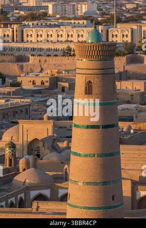 Il minareto di Juma sorge sopra i tetti e le strade sabbiose di Khiva Uzbekistan mentre il sole dorato tramonta sulla storica città vecchia. Foto Stock