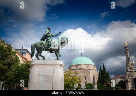 Statua equestre in bronzo di Janos Hunyadi comanda Piazza Szechenyi a Pecs, Ungheria, mentre l'ex moschea di Pascià Qasim - ora chiesa di candlemas - Foto Stock